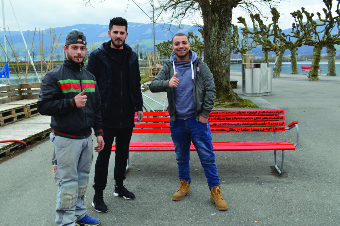 Three people beside a red bench.