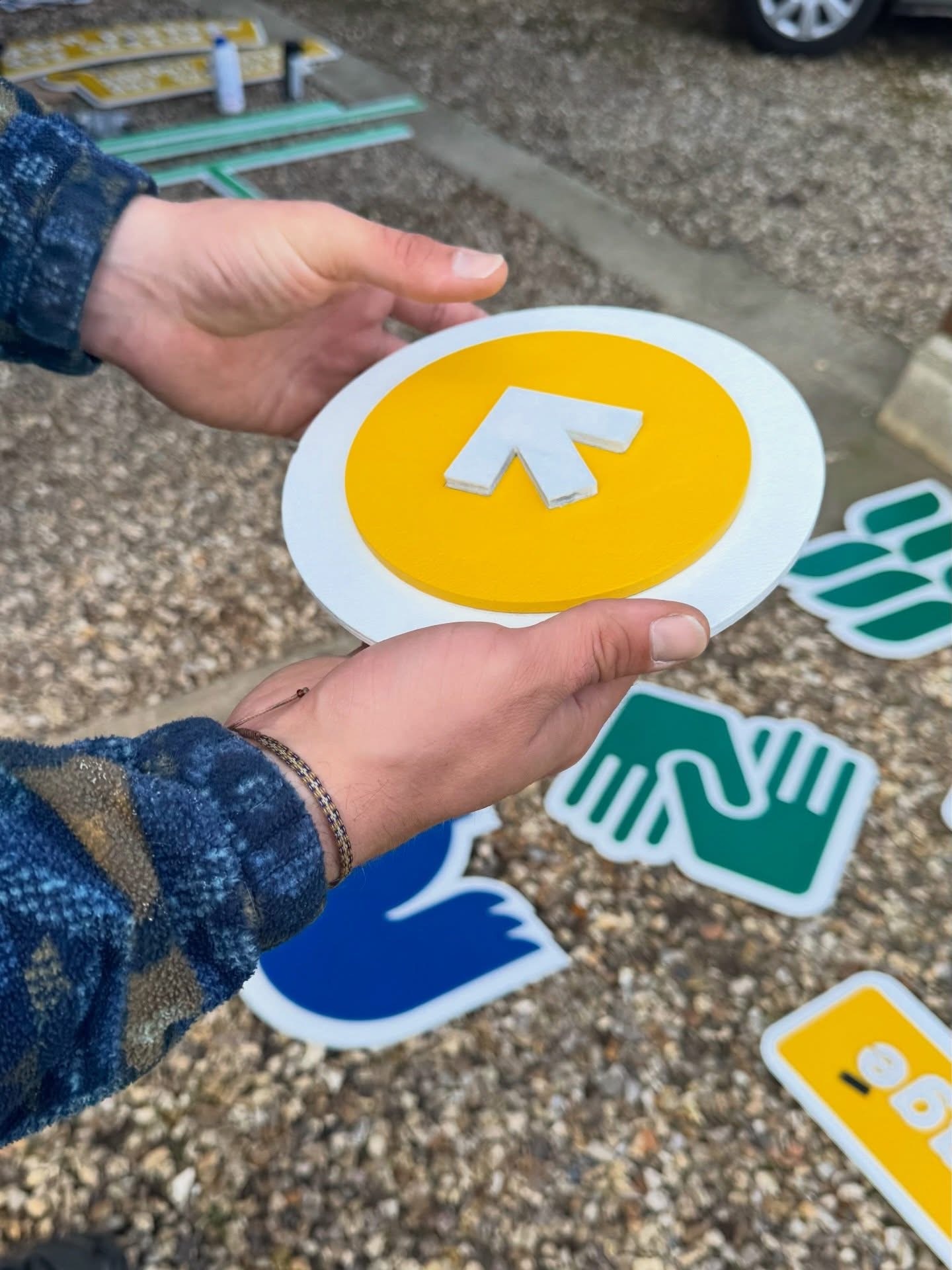 Mains avec un panneau fléché jaune.